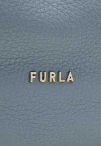 Jasnoniebieska sk�óra z teksturowaną powierzchnią, na której znajduje się nazwa marki "FURLA" w złotych metalowych literach.