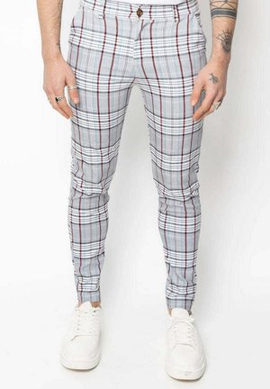 Pantalons à carreaux gris avec des lignes rouges et noires, taille mi-haute, coupe slim, dotés de passants de ceinture et de poches latérales. Associés à des baskets blanches.
