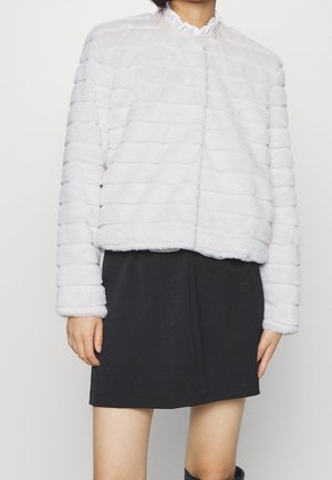 Woman wearing a white furry jacket with horizontal stripes over a black skirt, shown from shoulders to mid-thigh.