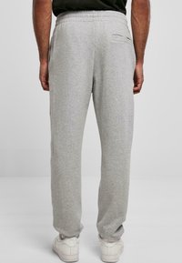 Szare spodnie dresowe z elastycznym paskiem w pasie, prostymi nogawkami i tylną kieszenią, zestawione z białymi trampkami. Miękki materiał bawełniany.