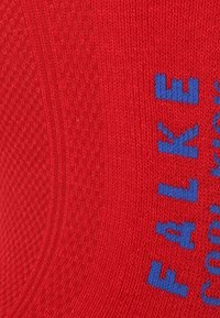 Rote gestrickte Socke mit strukturiertem Muster. Mit blauen Buchstaben, die "FALKE" deutlich auf der Oberfläche anzeigen.