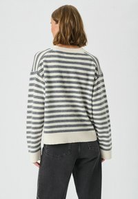 Sweter w paski w kolorze kremowym i szarym, charakteryzujący się luźnym krojem, ściągaczami na dolnym brzegu i rękawach, okrągłym dekoltem oraz opadającymi ramionami.
