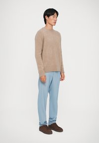 Bežinis megztinis, šviesiai mėlyni raišteliai, rudi sportbačiai. Minkšta tekstūra, laisvas kirpimas, subanguoti rankogaliai ir juosta ant megztinio.