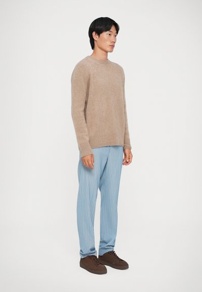 Pull en tricot beige, pantalon rayé bleu clair, baskets brunes. Texture douce, coupe décontractée, manches et taille côtelées sur le pull.