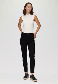 Witte geribde mouwloze top, gecombineerd met zwarte slim-fit broek en zwarte lichte sneakers, met een subtiele glans en een gestructureerde afwerking.