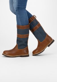 Bruna läder- och marinblå textil knähöga stövlar med platt sula, rund tå och dekorativa bruna remmar. Har en draglo plock i bak.