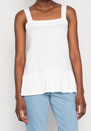 Weißes ärmelloses Oberteil mit eckigem Ausschnitt und gerafftem Saum, aus weichem Stoff gefertigt. Kombiniert mit hellblauen Jeans.