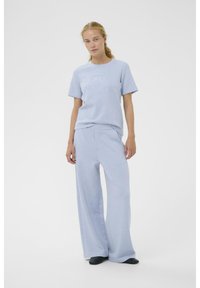 Hellblaues Baumwoll-T-Shirt mit kurzen Ärmeln und strukturiertem Logodesign, kombiniert mit passenden weiten Jogginghosen aus ähnlichem Material und in ähnlicher Farbe.