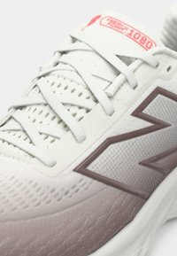 Chaussure de course pour homme avec une tige en mesh blanche et rose clair, présentant des détails texturés, des accents gris et un logo "N" bien visible.