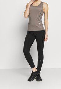 Grå ärmlös träningsskorta med meshanpassningar, parat med svarta åtsittande leggings och svarta träningsskor, vilket betonar komfort och flexibilitet.