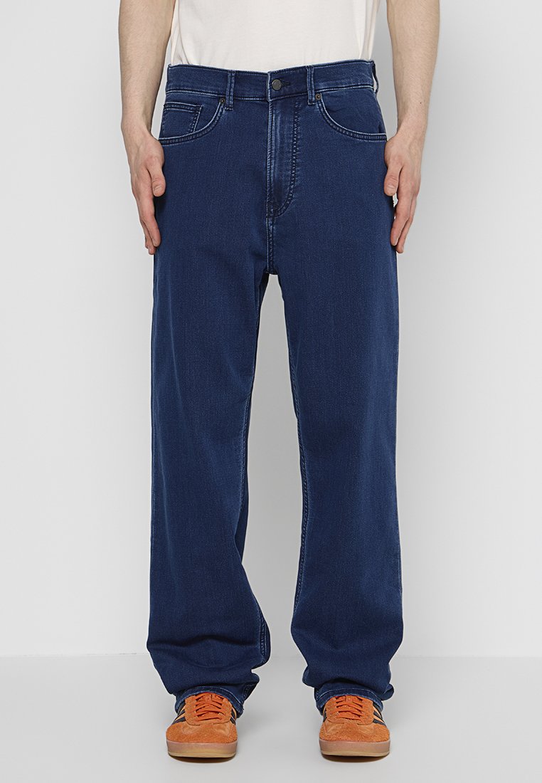 Jeans en denim bleu foncé avec une coupe relaxe, design à cinq poches et détails de couture subtils. Assortis à des baskets orange.