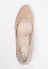Chaussure slip-on en cuir laqué nude avec un bout en amande, semelle intérieure rembourrée et détail de couture subtil sur le bord de la tige.