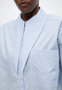 Ανοιχτό μπλε πουκάμισο με μοναδικό μυτερό γιακά, μία τσέπη στο στήθος και λεία υφή υφάσματος. Διαθέτει μοντέρνο σχεδιασμό και καθαρές γραμμές.