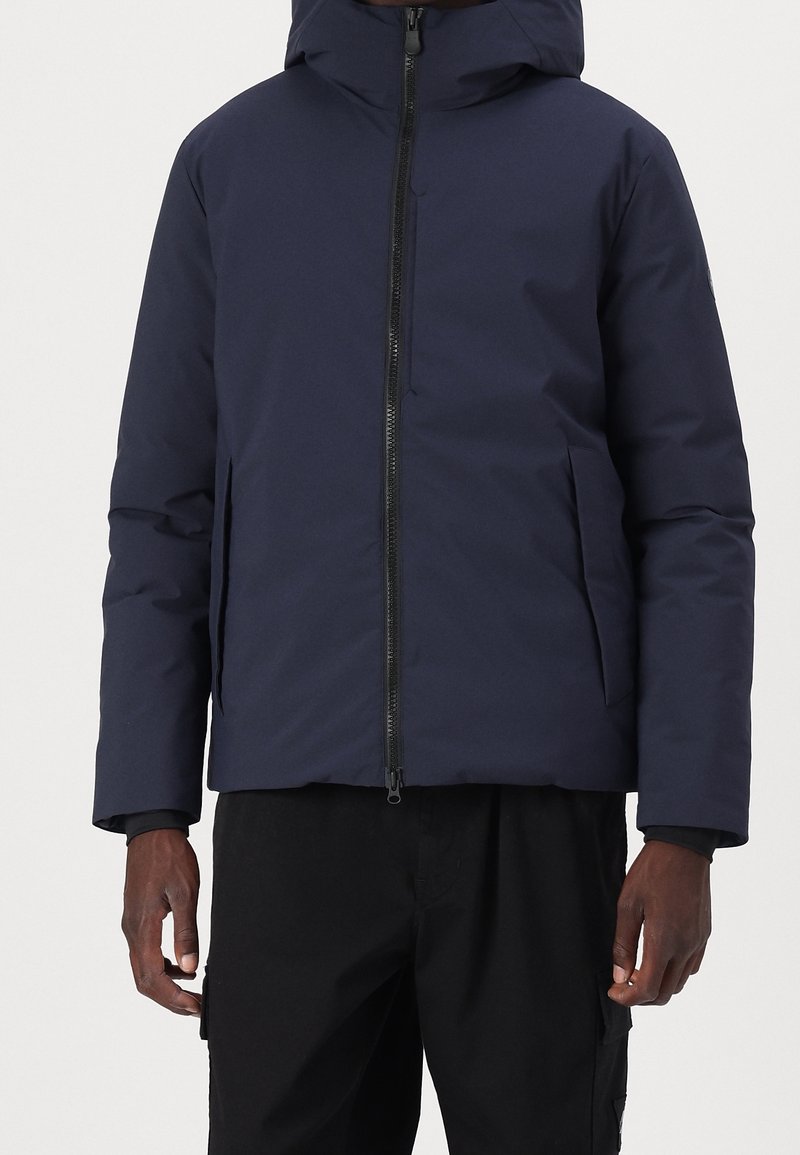 Mørkeblå vinterjakke med hætte, der har en frontlynlås og sidelommer. Glat tekstur og tætsiddende design med en skræddersyet silhuet.