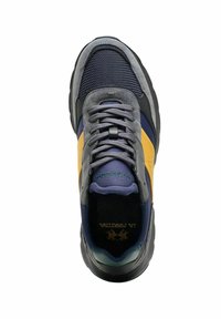 Zapatilla con parte superior de gamuza y malla gris, detalles en azul marino, franja lateral amarilla y suela de goma negra. Cuenta con cordones planos grises y lengüeta acolchada.