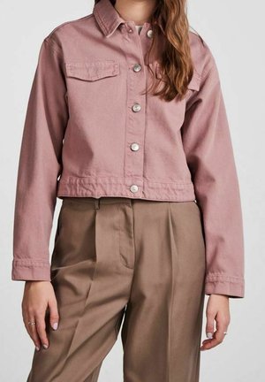 Woman wearing a cropped dusty pink button-up jacket with chest pockets and high-waisted brown pleated trousers.