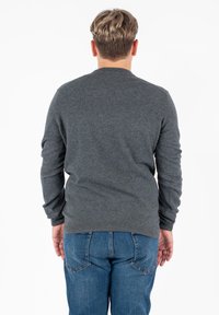 Maglione grigio a maglia con scollatura rotonda e maniche lunghe, indossato su jeans in denim blu. Il tessuto sembra morbido e di peso medio.
