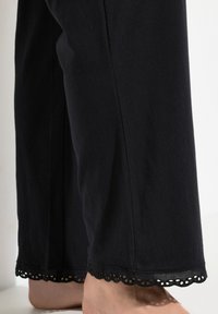 Pantalones de algodón negros con un dobladillo de encaje en forma de concha. La textura es suave, con un ajuste relajado y sin adornos adicionales.
