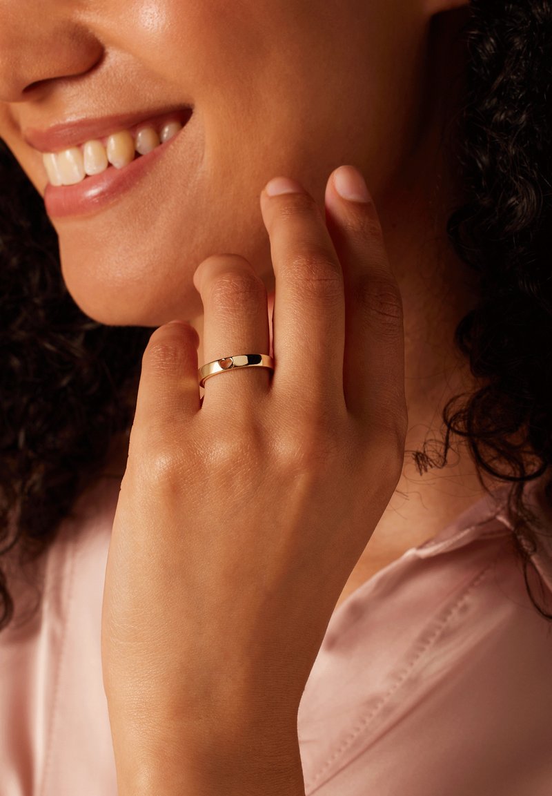 Gold ring with a polished finish and a heart-shaped accent, worn on a finger, showcasing a smooth design and elegant simplicity.