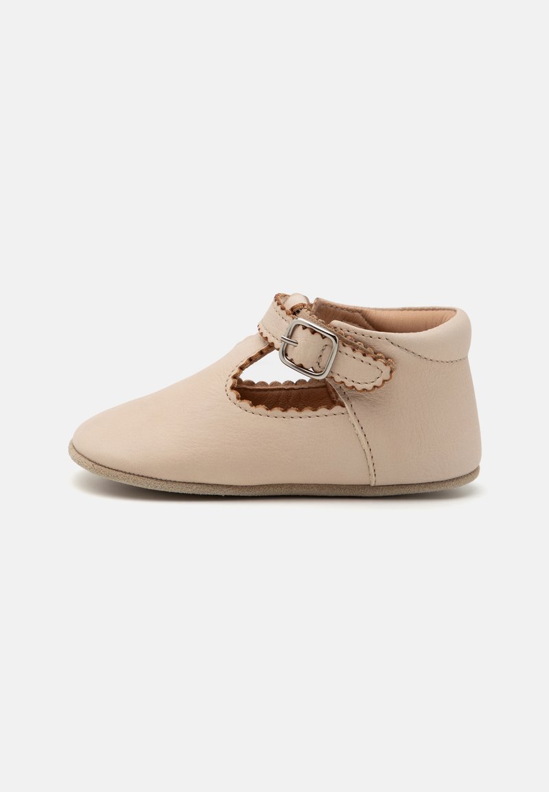 Beige leather shoe with a rounded toe, cut-out accents, and a buckle strap across the ankle. Smooth texture with stitched detailing.