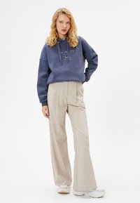 Outfit con felpa e pantaloni a gamba larga. Felpa in cotone blu con testo grafico, abbinata a pantaloni in tessuto beige e sneakers bianche. Design semplice.