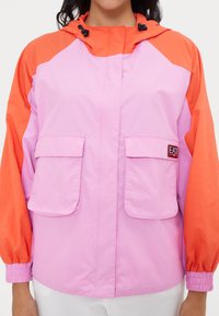 Color-blocked jacket with a pink body and orange sleeves, made of lightweight material, featuring a hood and two front pockets.