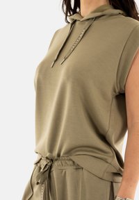 Top sin mangas en verde oliva, confeccionado en tejido suave, con cordones y un corte relajado, combinado con pantalones a juego con cordones.