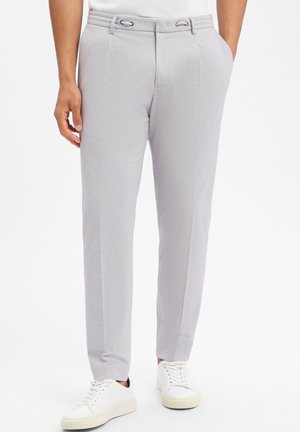 Hellgraue, maßgeschneiderte Hose mit Seitentaschen, getragen von einer stehenden Person, kombiniert mit weißen Sneakern mit niedrigem Schaft.