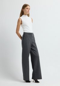 Top blanco sin mangas de cuello alto combinado con pantalones anchos gris. Los pantalones presentan un sutil patrón de rayas y bolsillos delanteros. Tacones negros de punta.