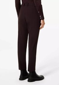 Personne portant un pantalon ajusté marron foncé, de longueur cheville, associé à des bottes noires à semelle épaisse, vu de dos.