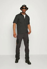 Melna īsām piedurknēm krekls ar pus-pievilcēju, apvienots ar tumšiem kravas biksēm ar kabatām un melniem zābakiem. Aksesuāri iekļauj melnu cepuri un saulesbrilles.