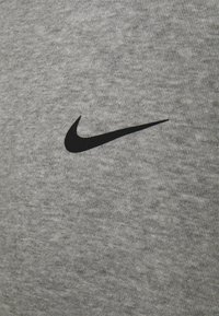 Šedá bavlněná tkanina s hladkou texturou má výrazné černé logo Nike umístěné na levé straně.