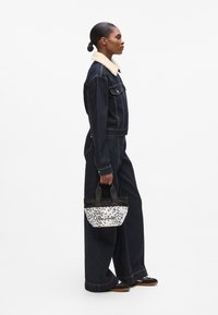 Denim jacket with a faux fur collar, paired with wide-leg denim pants. Holding a black and white patterned handbag with short handles.