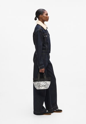 Giacca in denim con collo in pelliccia sintetica, abbinata a pantaloni in denim a gamba larga. Tiene una borsa a tracolla con un motivo in bianco e nero e manici corti.