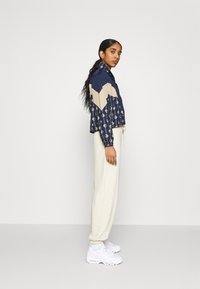 Giacca accorciata navy e crema con motivo geometrico e orlo regolabile, abbinata a jogger crema e sneakers bianche.