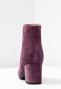 Lilla ruskindsankelstøvle med en kraftig hæl, glat tekstur, afrundet tå og et enkelt design. Bagfra, ingen yderligere detaljer synlige.