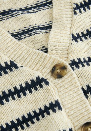 Pleteni kardigan v kremni barvi z mornarskimi črtami. Ima V-izrez in gumbasto zapiranje, mehak videz ter vidne rebraste detajle.