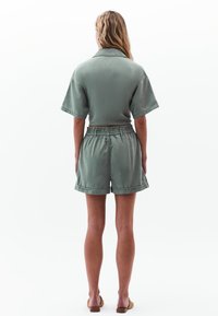 Groene katoenen T-shirt met korte mouwen en bijpassende shorts met elastische tailleband, met een relaxte pasvorm en omgeslagen zomen, gezien vanuit de achterkant.