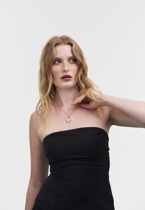 Must musta top koos struktureeritud disainiga, millel on kuldne kaelakee ümmarguse ripatsiga. Modellil on lainelised blondid juuksed ja neutraalne meik.