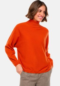 Pull à col roulé orange en matière douce, doté de manches longues et d'une coupe décontractée, associé à un pantalon à carreaux.