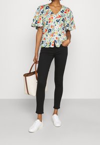 Květinový top s krátkým rukávem a výstřihem do V, s vícebarevným vzorem na světlém pozadí; v kombinaci s černými slim-fit kalhotami a bílými teniskami.