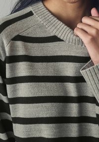 Pull rayé gris et noir avec un col en v côtelé, présentant une texture douce et une coupe ample, visible au niveau de l'encolure et des épaules.