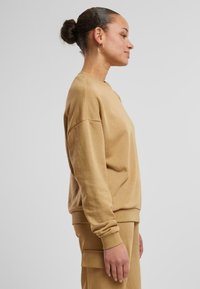 Khakifarbener Sweatshirt mit Rundhalsausschnitt, lockerer Passform und gerippten Bündchen. Weiche Textur; ergänzt durch passende Hosenmerkmale, die sichtbar sind.