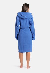 Blauwe katoenen badjas met een capuchon, geknoopte taille, lange mouwen en een textuurafwerking. Witte accenten op de schouders.