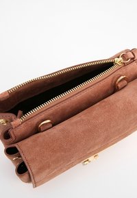 Braune Wildleder-Handtasche mit einem Reißverschlussverschluss, goldfarbenen Beschlägen und einem geräumigen Innenraum mit strukturiertem Design.