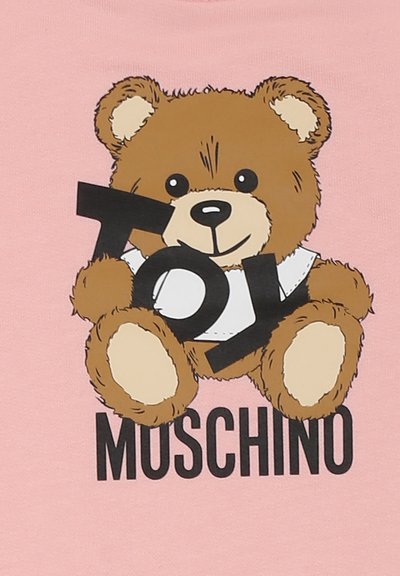 T-shirt rosa con un orsetto dei cartoni animati che tiene un blocco con la scritta nera "Toy" e il testo "Moschino" sottostante in grassetto nero.