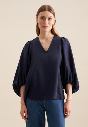 Marineblouse met V-hals, gathered puff sleeves en een ontspannen pasvorm. Gemaakt van soepele stof met een subtiele glans. Gecombineerd met denim.