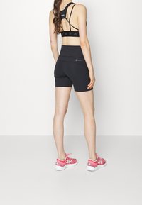 Černé atletické krátké šortky s vysokým pasem, doplněné o sladěnou černou sportovní podprsenku se šňůrkovým designem na zádech a růžové atletické boty.