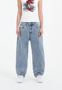 Light blue, oversized denim jeans with a high waist and wide legs. Features front pockets and a faded wash. Paired with a white graphic t-shirt.