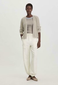 Cárdigan de punto beige sobre una camiseta gris con bordes azules, combinado con pantalones cargo cremosos y zapatillas ligeras grises. Diseño sencillo y relajado.